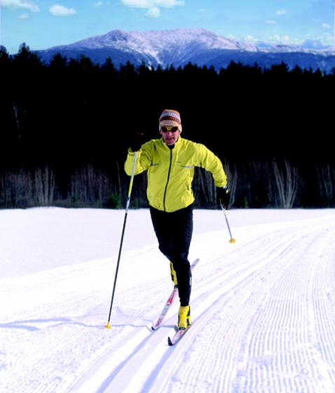 Skier in yellow jacket on a snowy trail, with mountains in the background.