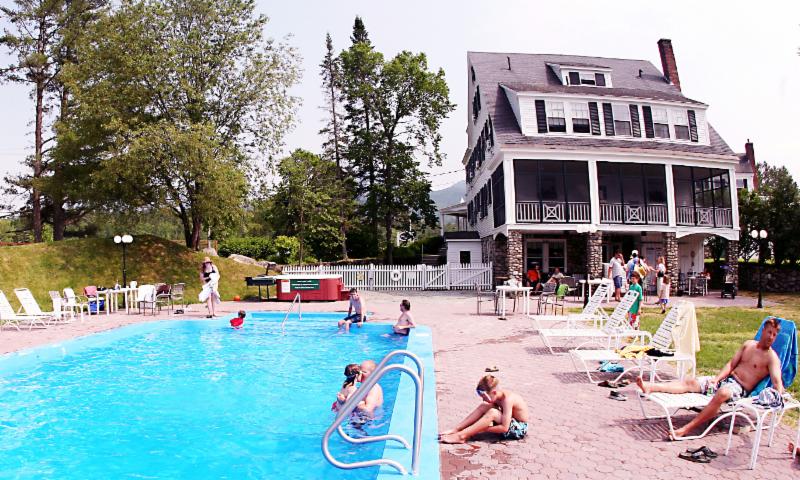Pool with people, a large white building with a porch, outdoor setting, sunny day.