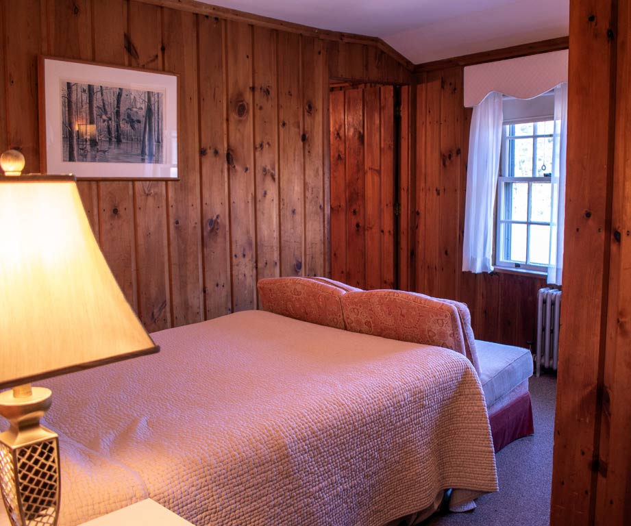 Bedroom with wood paneling, bed, small window, and lit lamp.