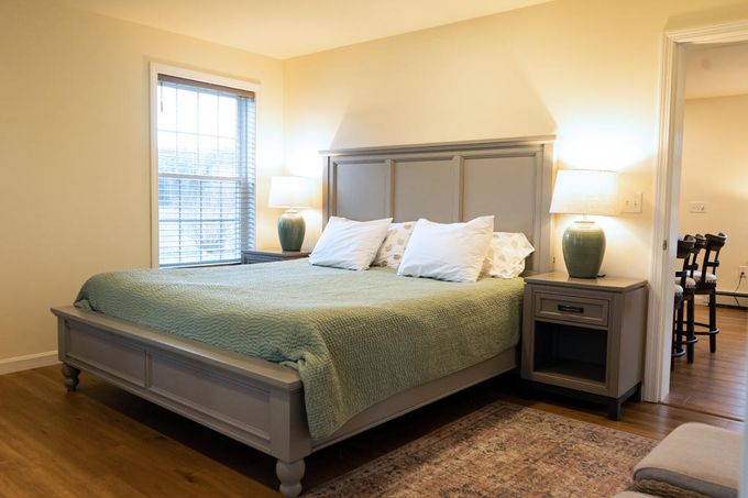 Bedroom with a gray bed, two nightstands, a window, and an open doorway.