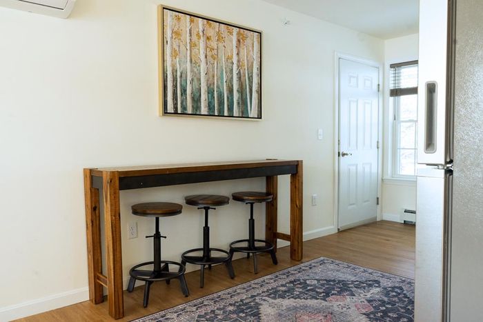 Rustic wooden table with three stools, an abstract art piece, and a rug in a room with a door.