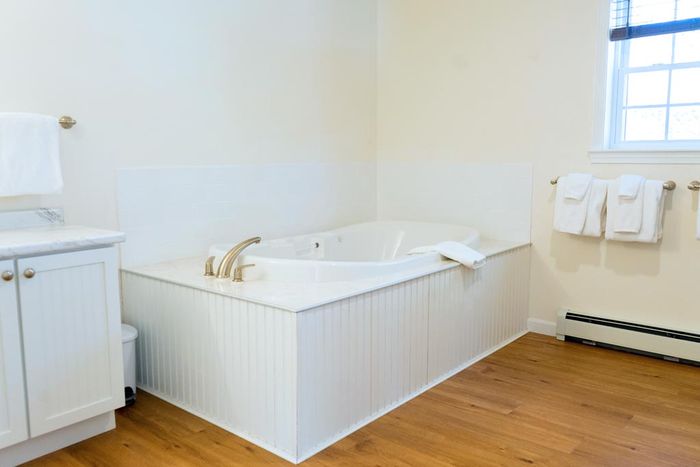Bathroom with a white jetted tub, white cabinets, and hardwood floors.