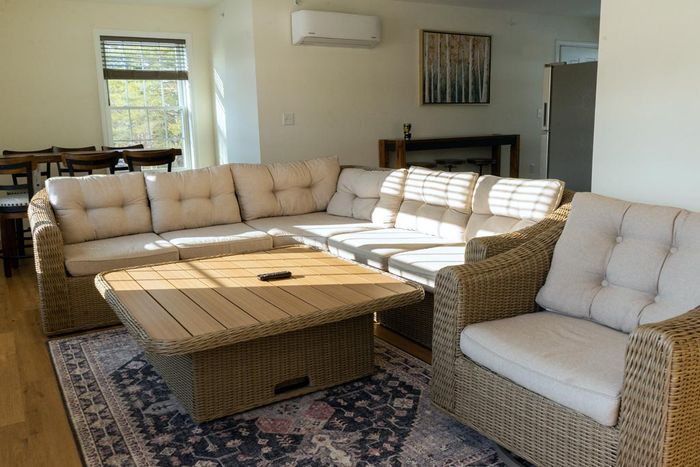 Lounge area with wicker sectional sofa, armchair, and coffee table on a patterned rug; bright, natural light.