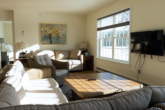 Cozy living room with, large windows, and neutral-toned furniture, including a sofa, loveseat, and coffee table.