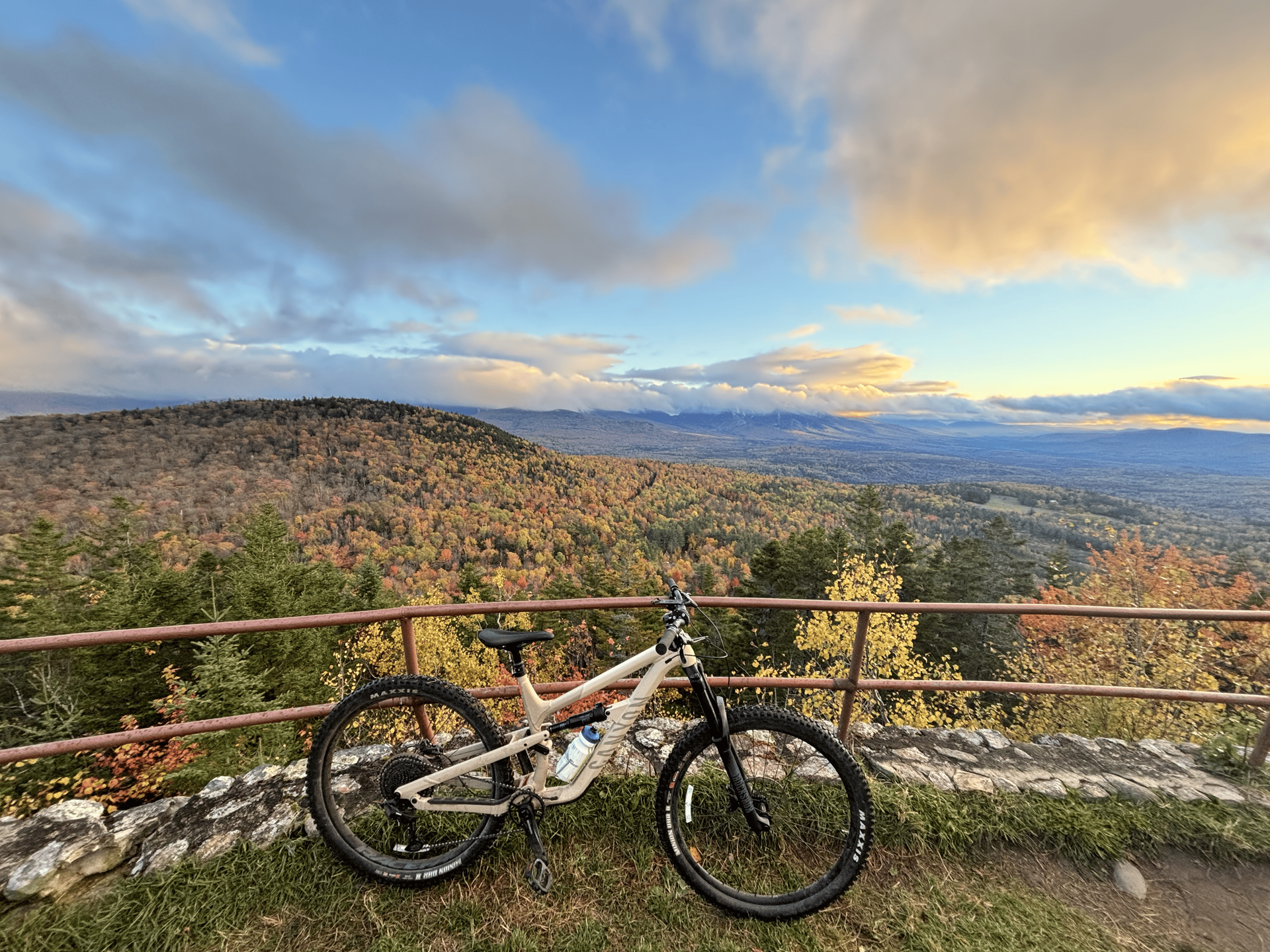 Mountain bike by a railing overlooking a rocky valley at sunset under a cloudy sky