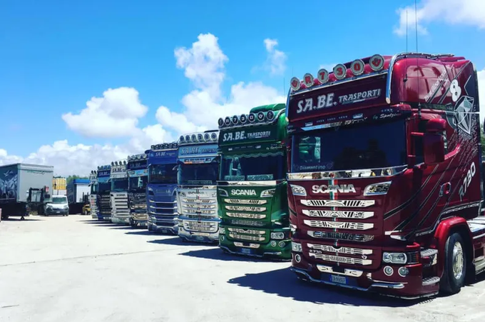 Una fila di coloratissimi camion parcheggiati in un piazzale soleggiato sotto un cielo azzurro.