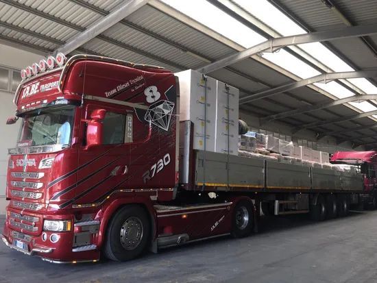 Autocarro rosso con rimorchio a pianale all'interno di un magazzino coperto o di una banchina di carico.