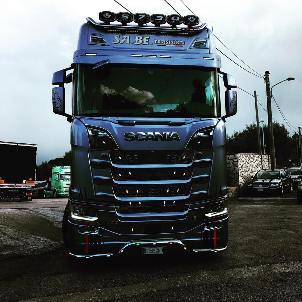 Vista frontale di un semirimorchio Scania blu su strada, con luci sul tetto e dettagli cromati.