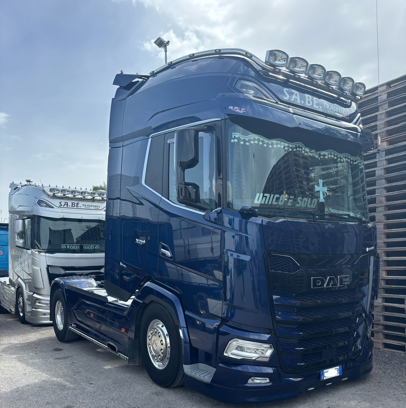 Un semirimorchio blu scuro è parcheggiato all'aperto, con un altro camion alle sue spalle.