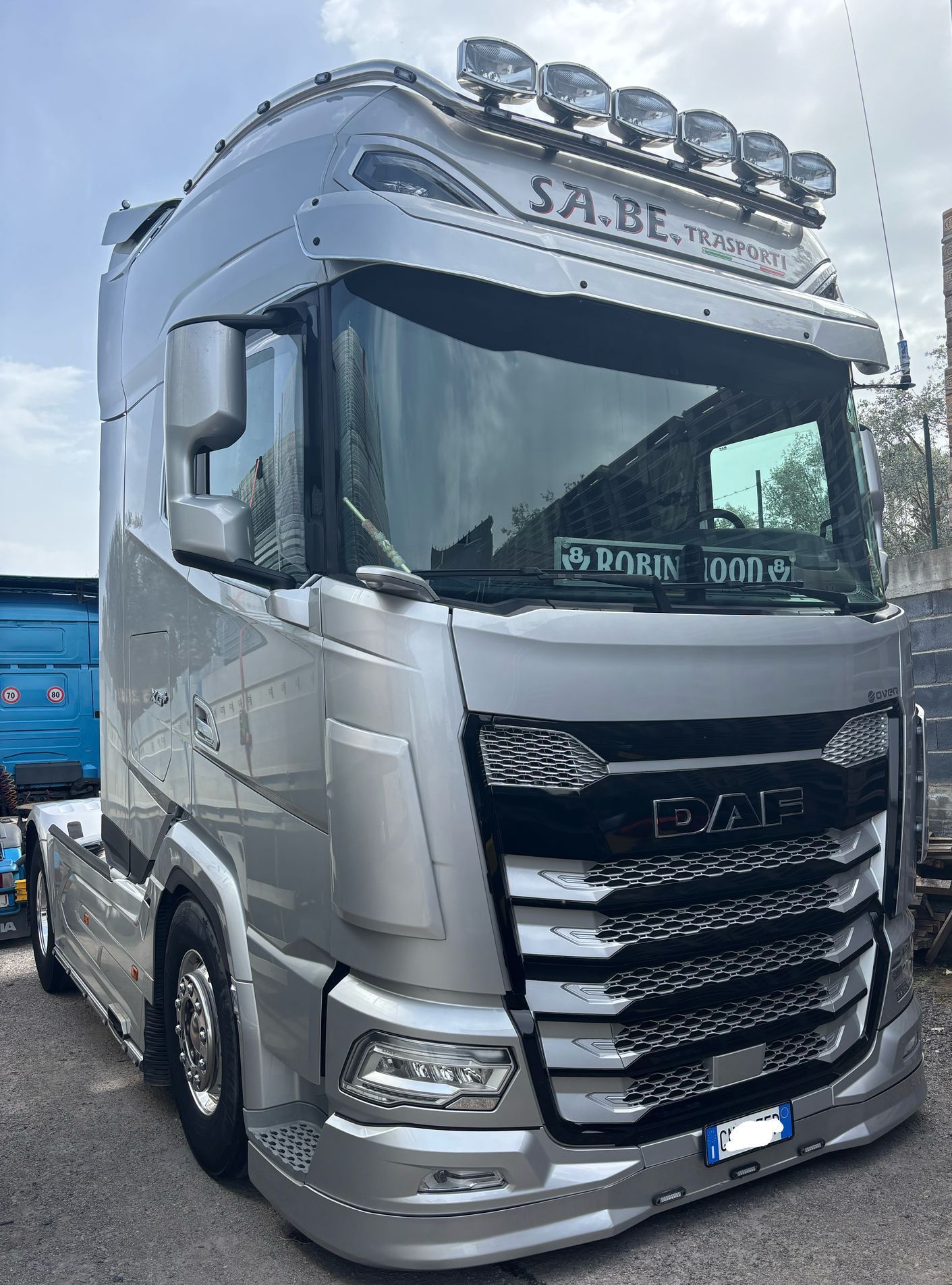 Autocarro Scania color argento parcheggiato all'aperto, vista frontale con dettagli cromati e luci sul tetto.