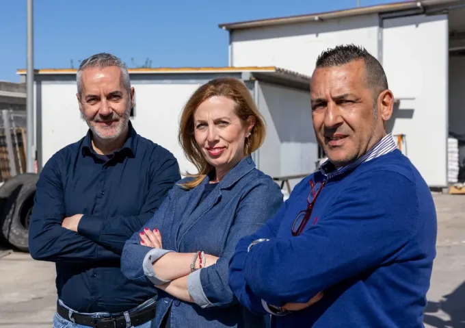 In pieno giorno, tre persone sono in piedi con le braccia incrociate davanti a un edificio.