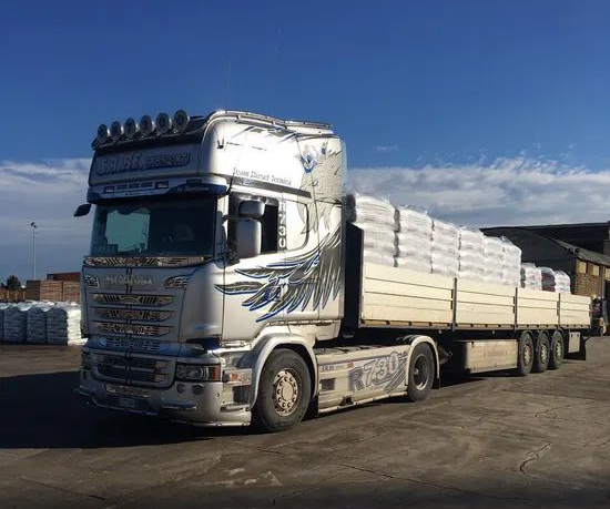 Un camion bianco che trasporta rimorchi bianchi impilati su una strada sotto un cielo azzurro
