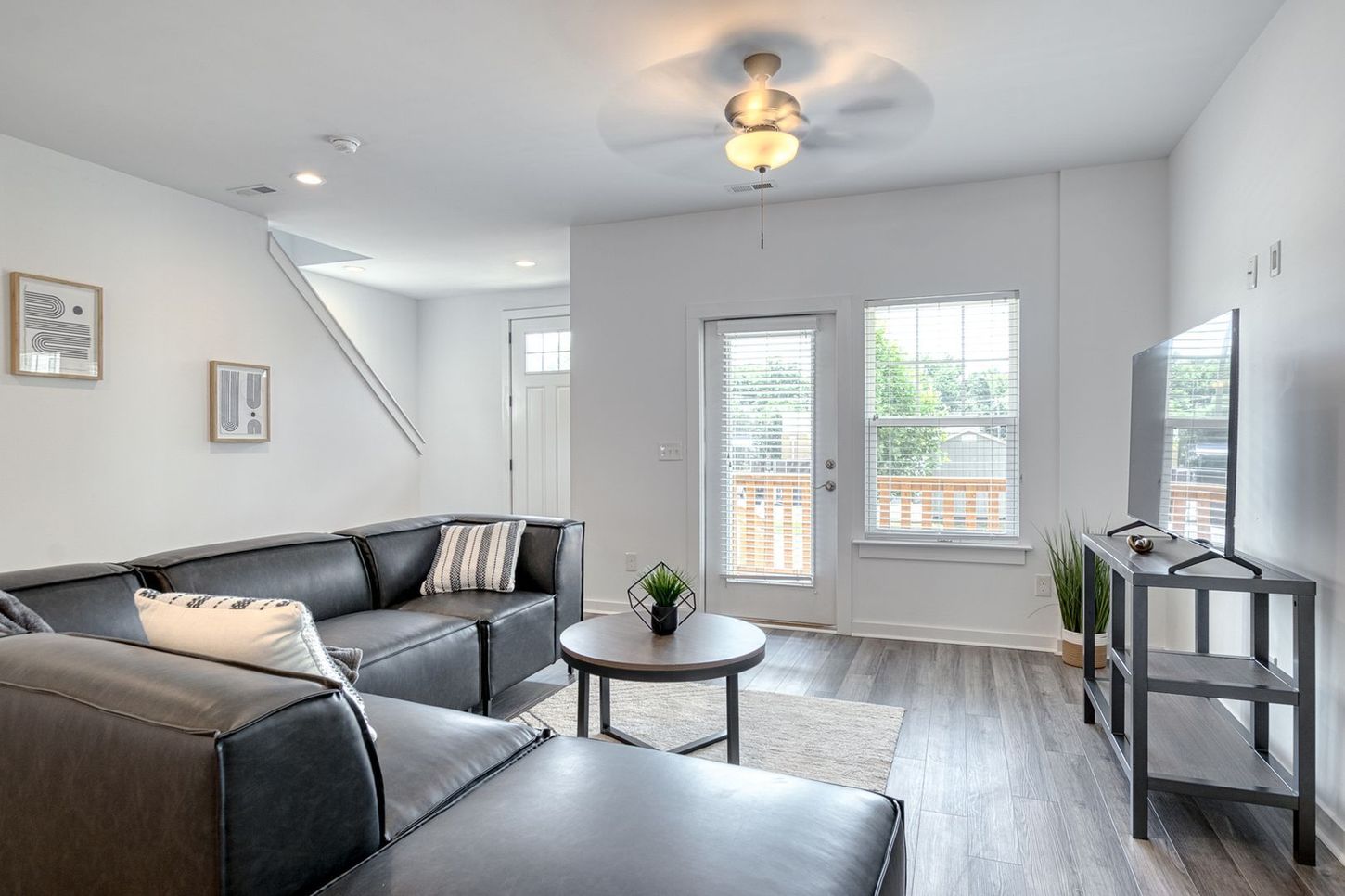 Modern living room with black sectional sofa, round coffee table, TV, and access to a balcony.
