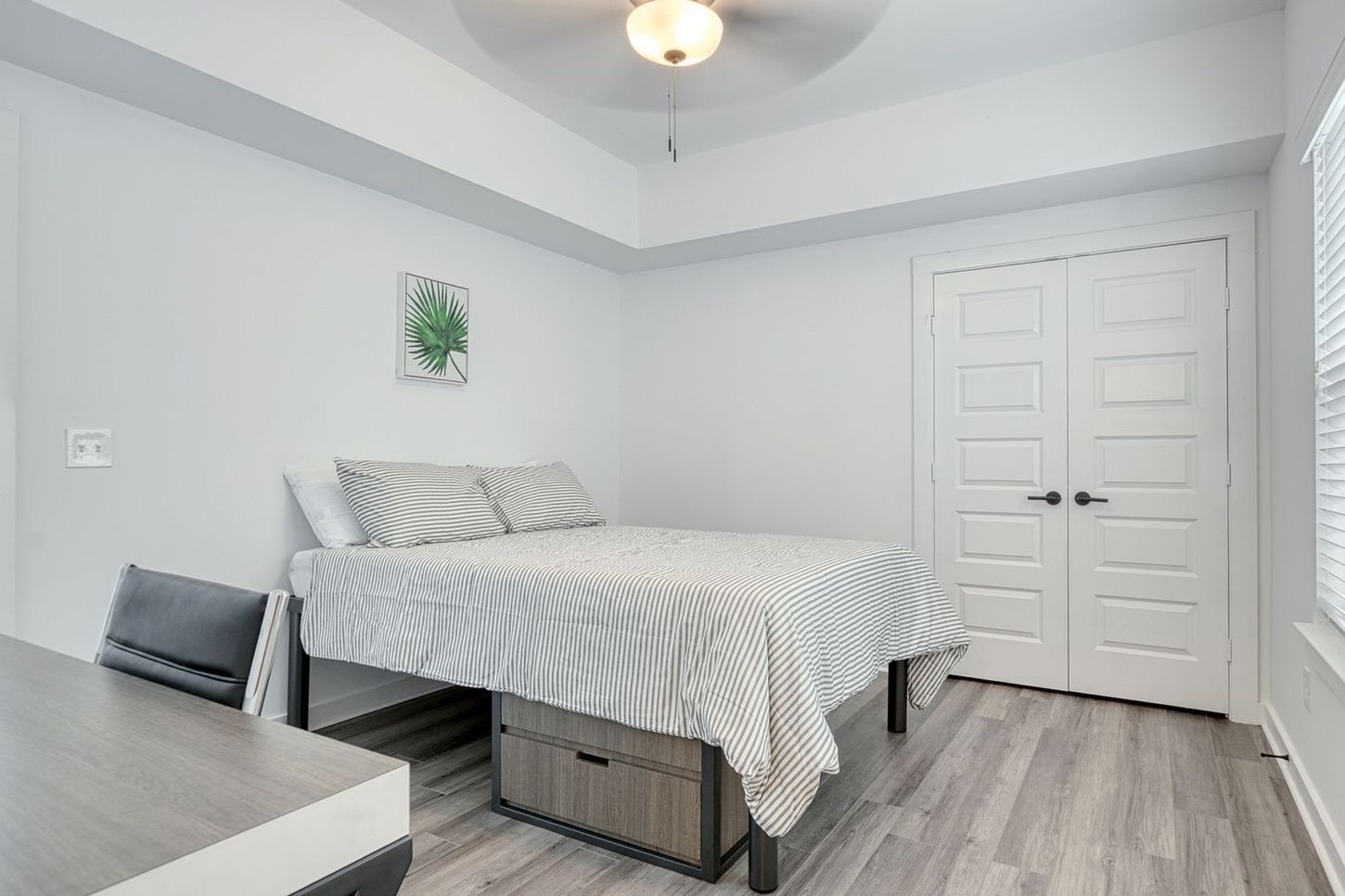 Bedroom with a bed, desk, closed doors, and a window with blinds.