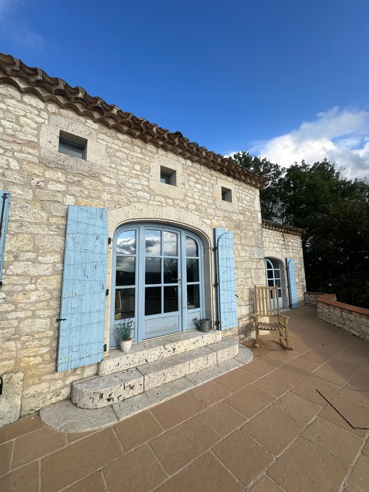Maison en pierre avec volets et porte bleus, petit patio, ciel bleu.