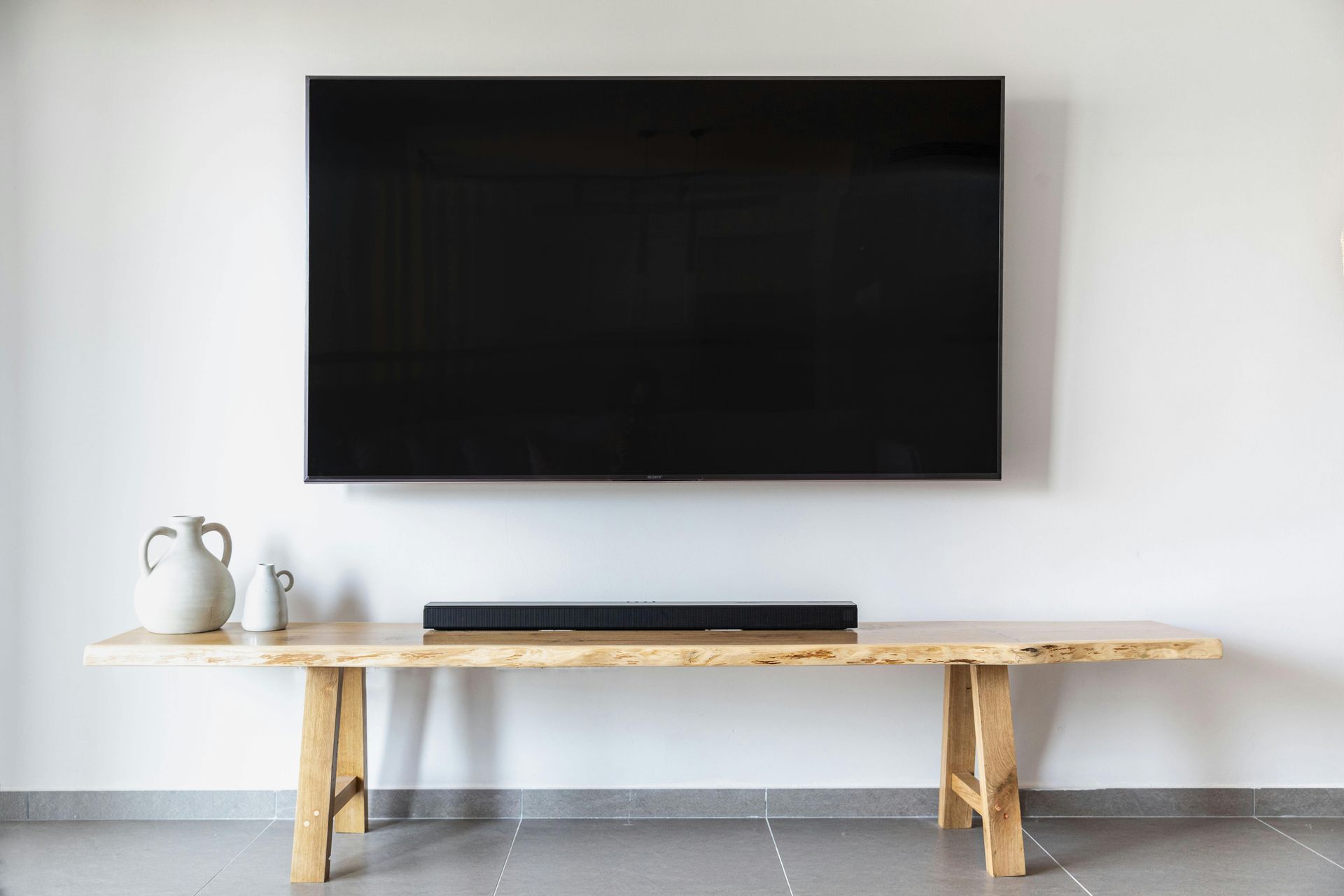 Minimalist living room with wall-mounted TV above a rustic bench on a white wall and gray floor