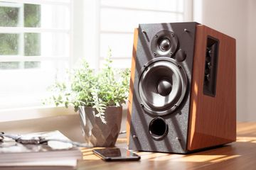 Black speaker on a wooden table beside a vase of flowers in a sunlit room