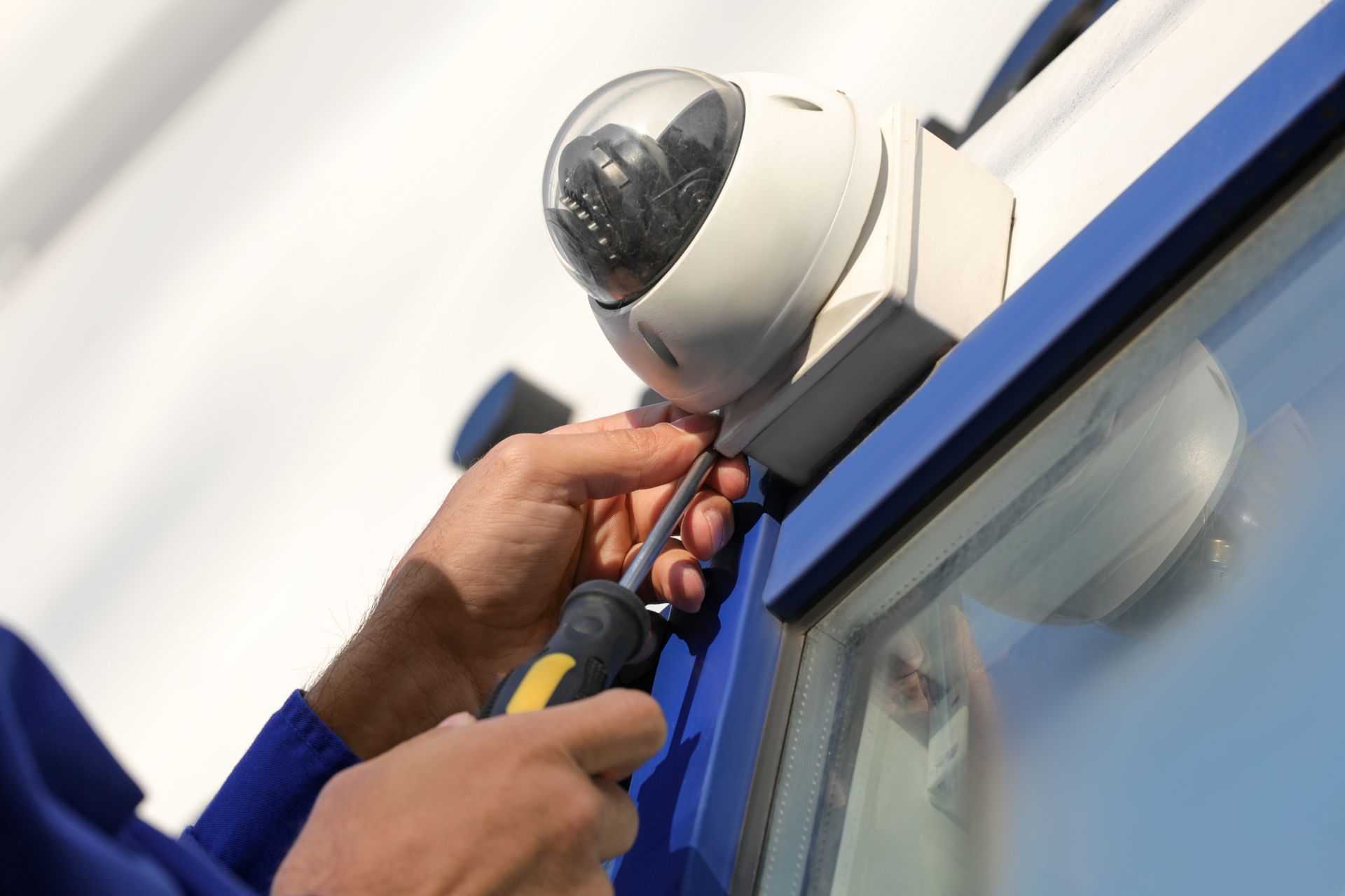 Technician installing a security camera on a blue building wall with a screwdriver