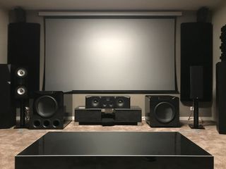 Home theater with large projector screen, black speakers, and subwoofers on a carpeted floor.