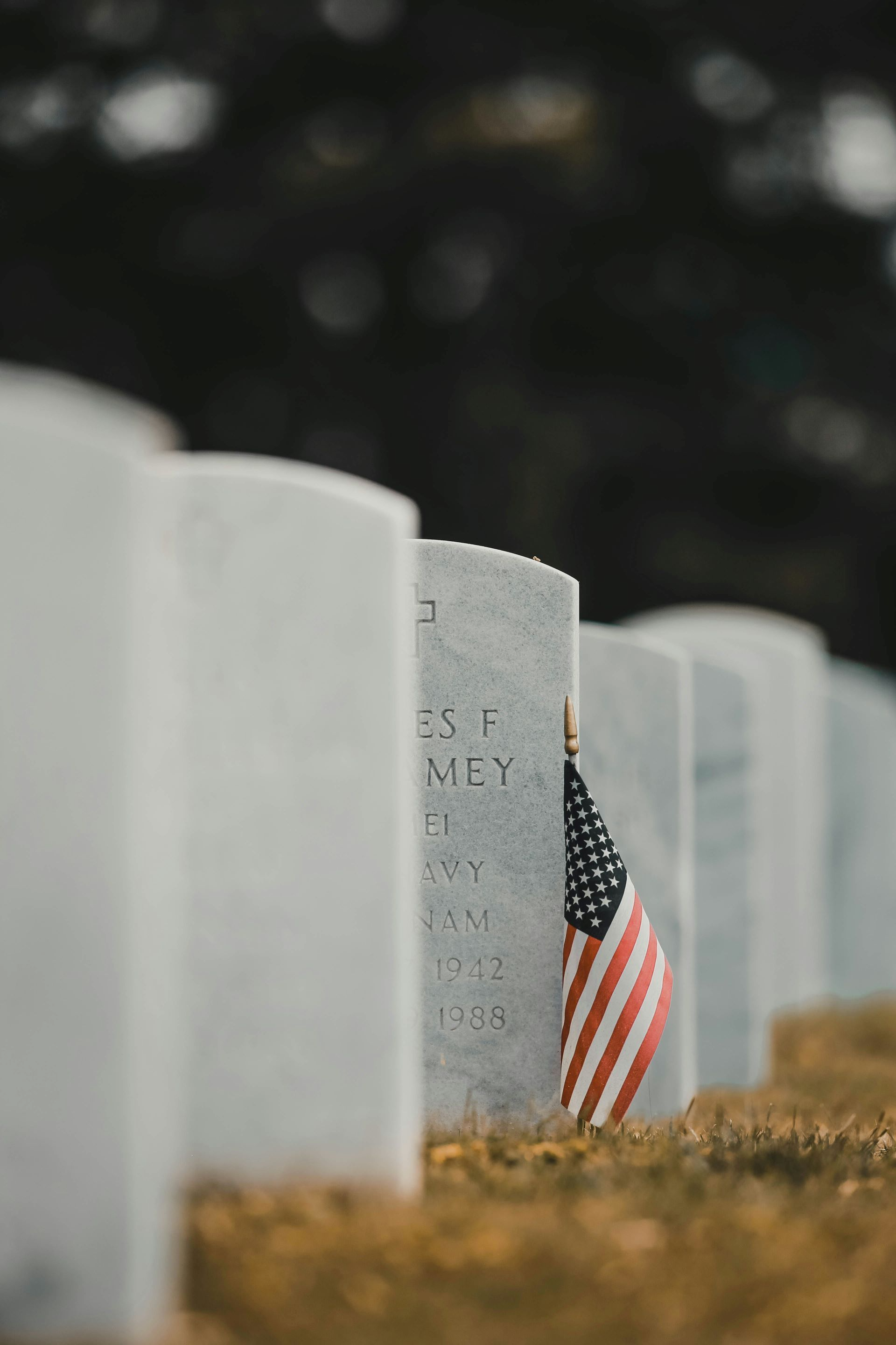 Rows of white gravestones with an American flag at a cemetery memorial.