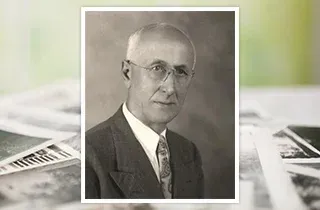Black-and-white portrait of a man in a suit and tie with glasses, framed over a blurred background
