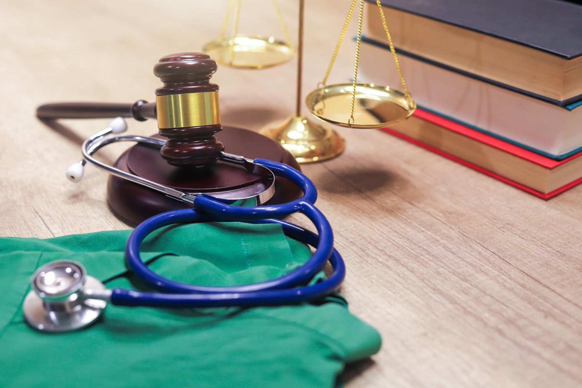 A stethoscope is sitting on top of a green scrub next to a gavel and scales of justice.