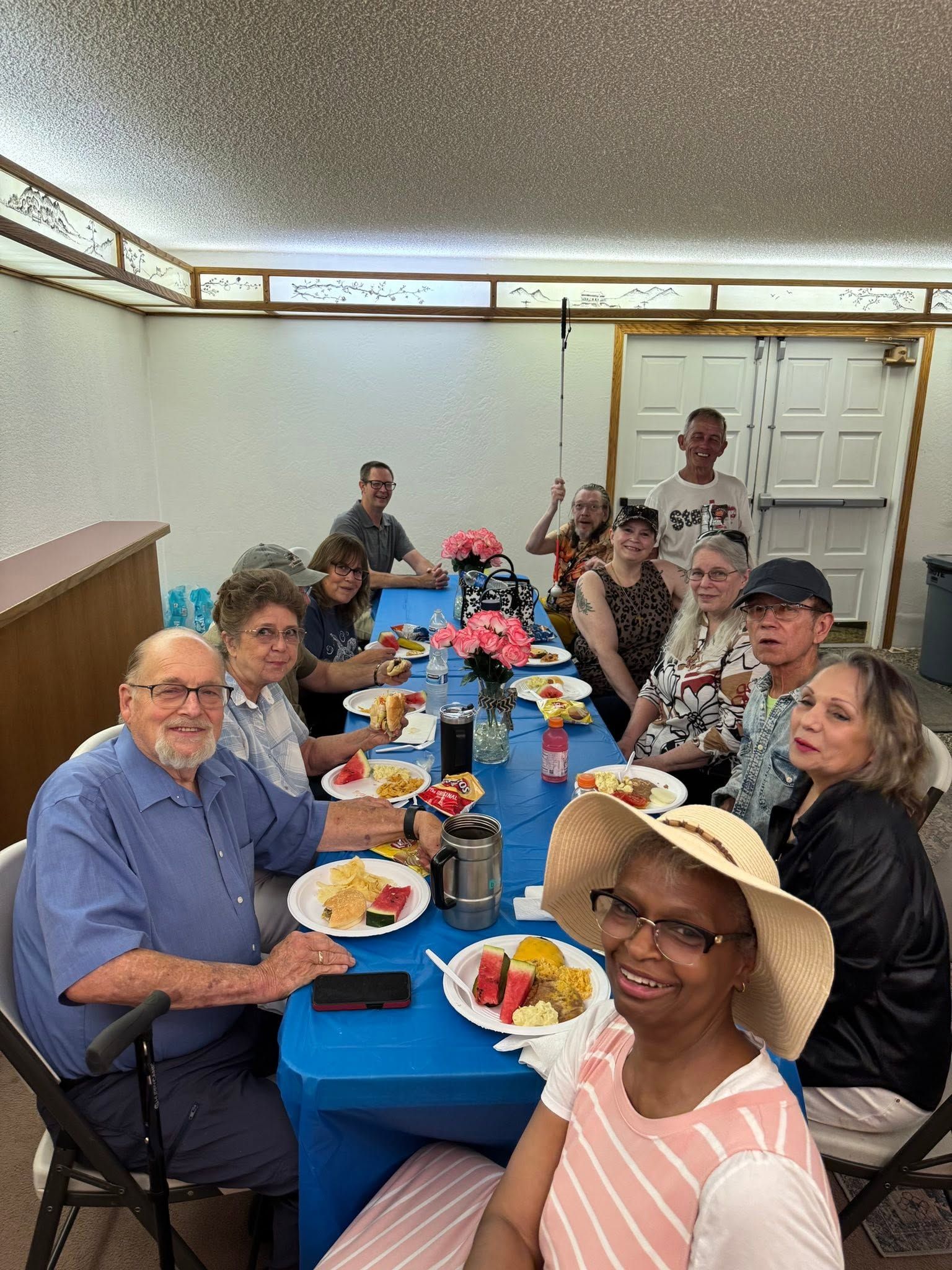 People seated at a long blue table sharing a meal in a dining room, smiling and posing for the camera.