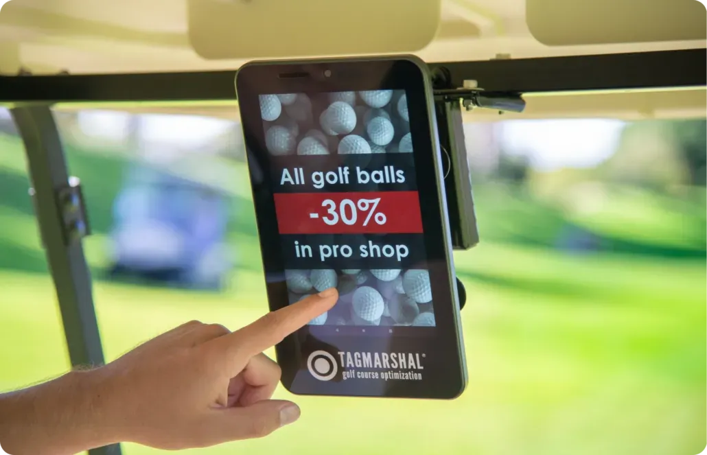 Hand touching a tablet in a golf cart displaying a 30% golf shop sale ad