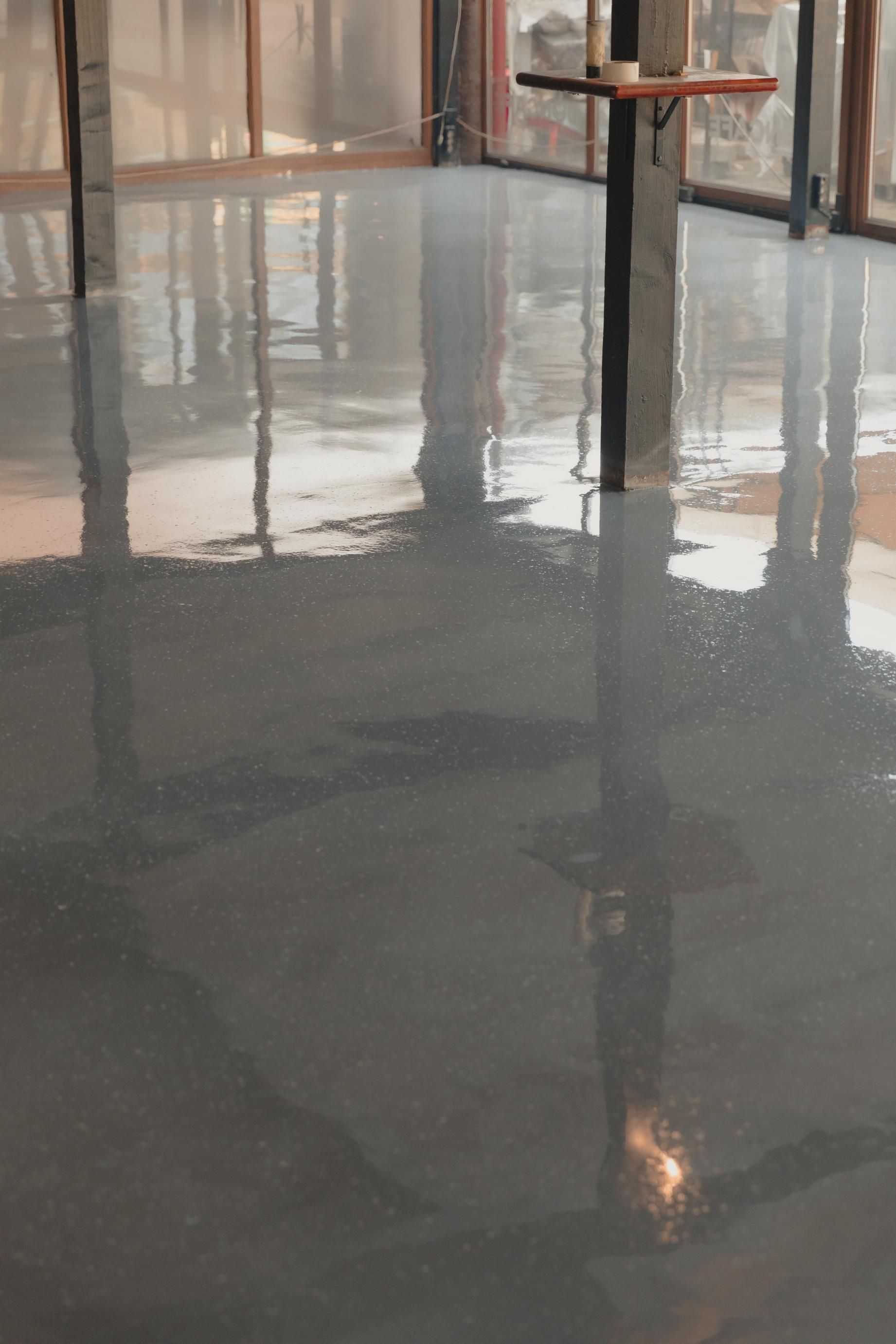 Shiny, gray epoxy floor reflecting interior room with pillars and windows.