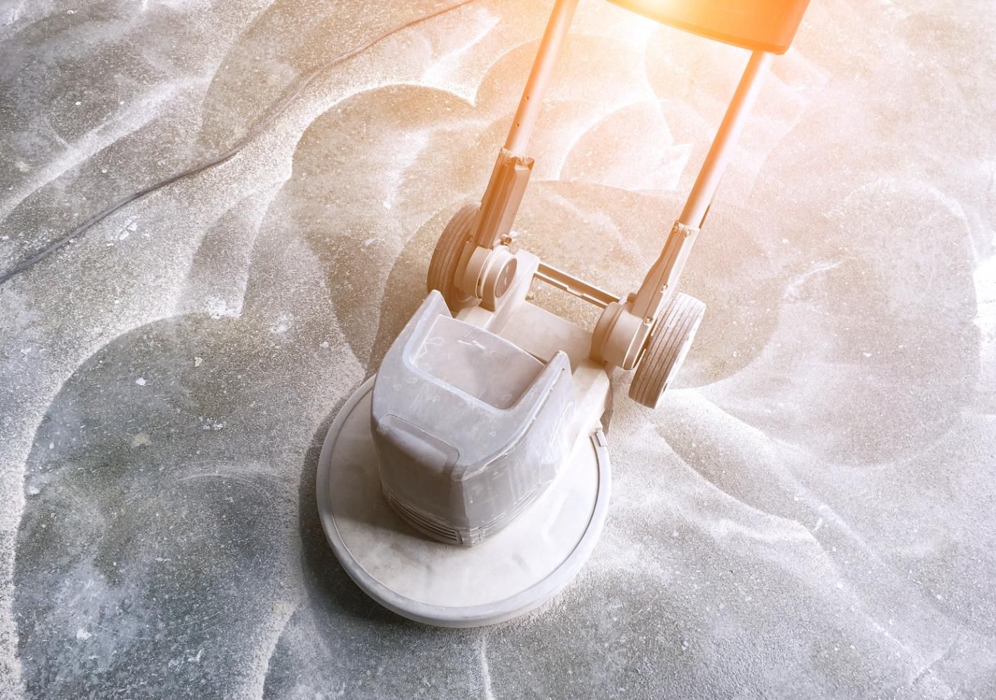 Floor buffer cleaning a gray surface, with a bright light reflecting.