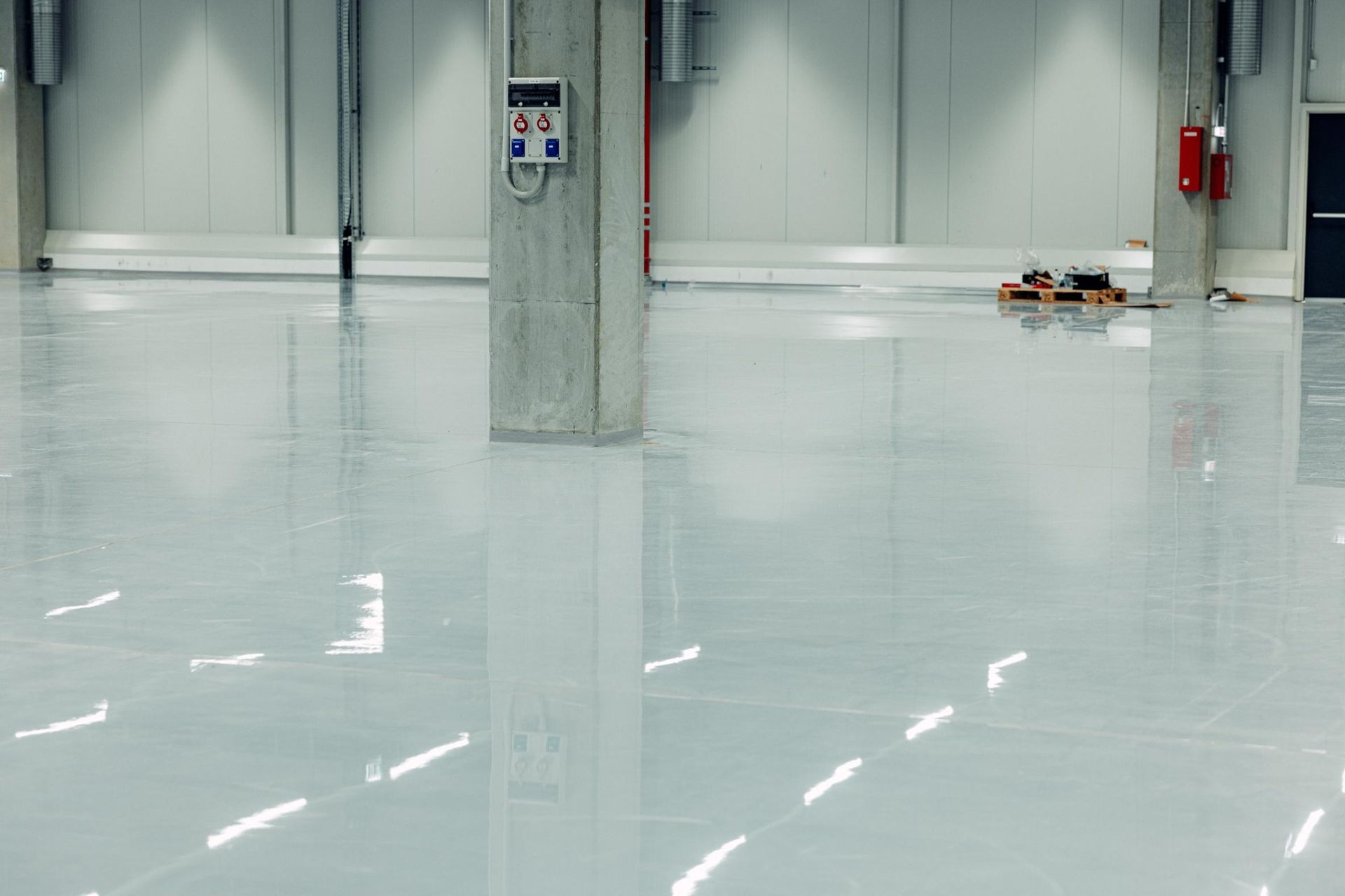 Shiny, white industrial floor reflecting the overhead lights, pillars, and walls.