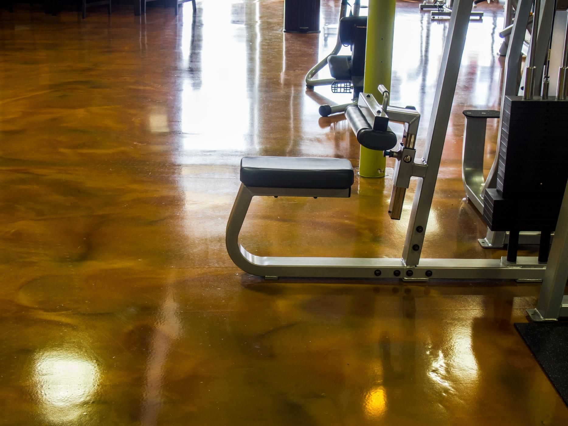 Gold-colored, glossy epoxy floor in a gym, reflecting light and weight-training equipment.