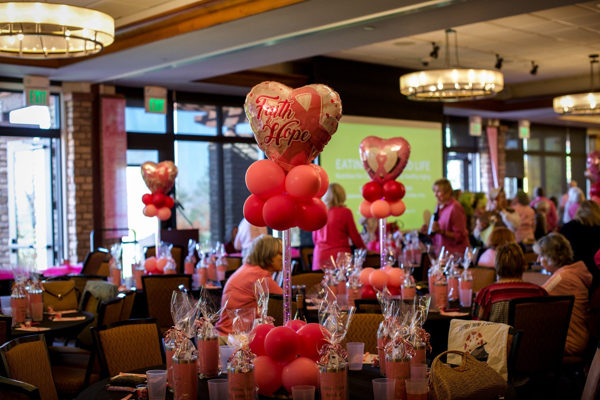 A group of people are sitting at tables decorated with pink balloons.