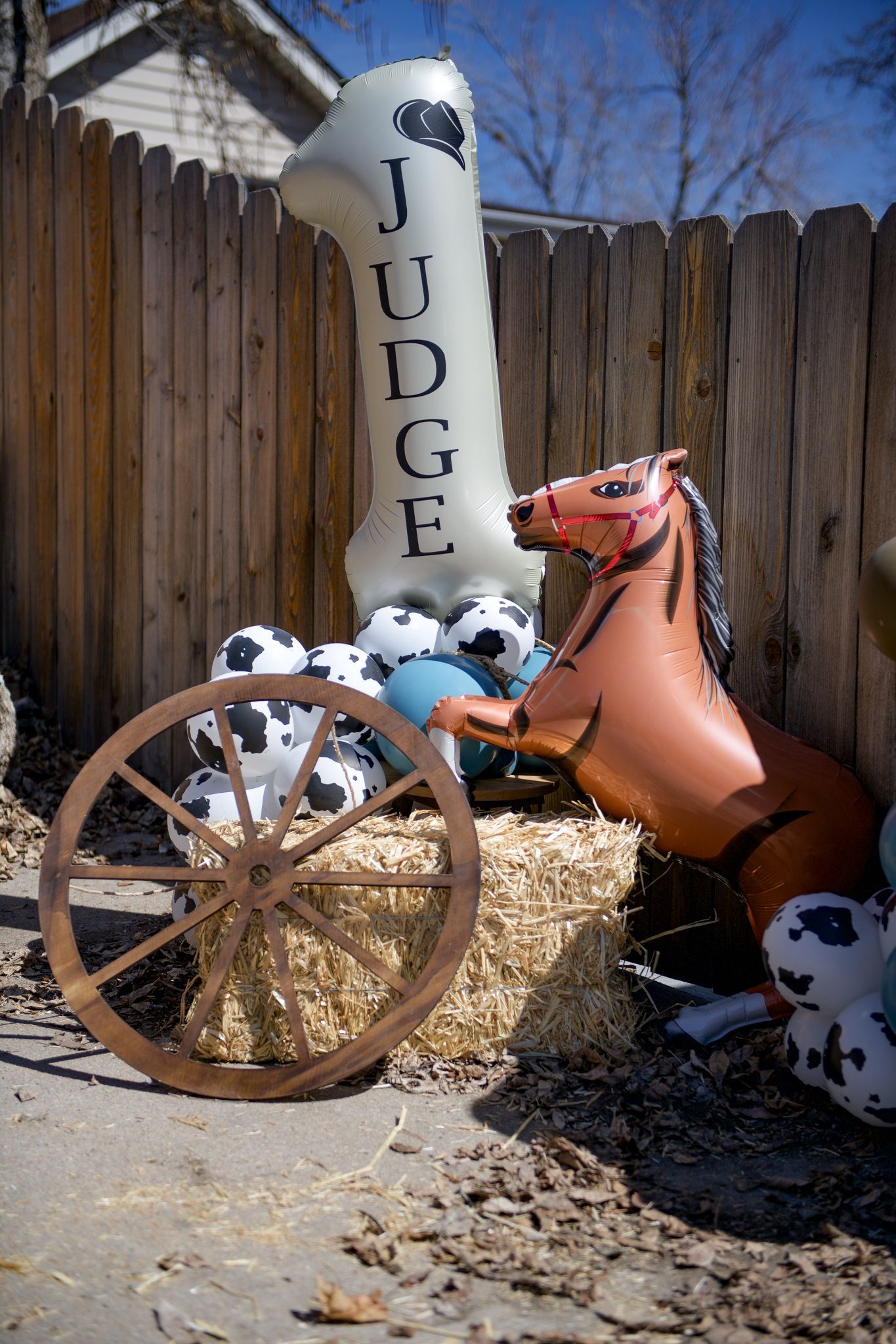 A horse shaped balloon is sitting on top of a hay bale next to a wagon wheel.