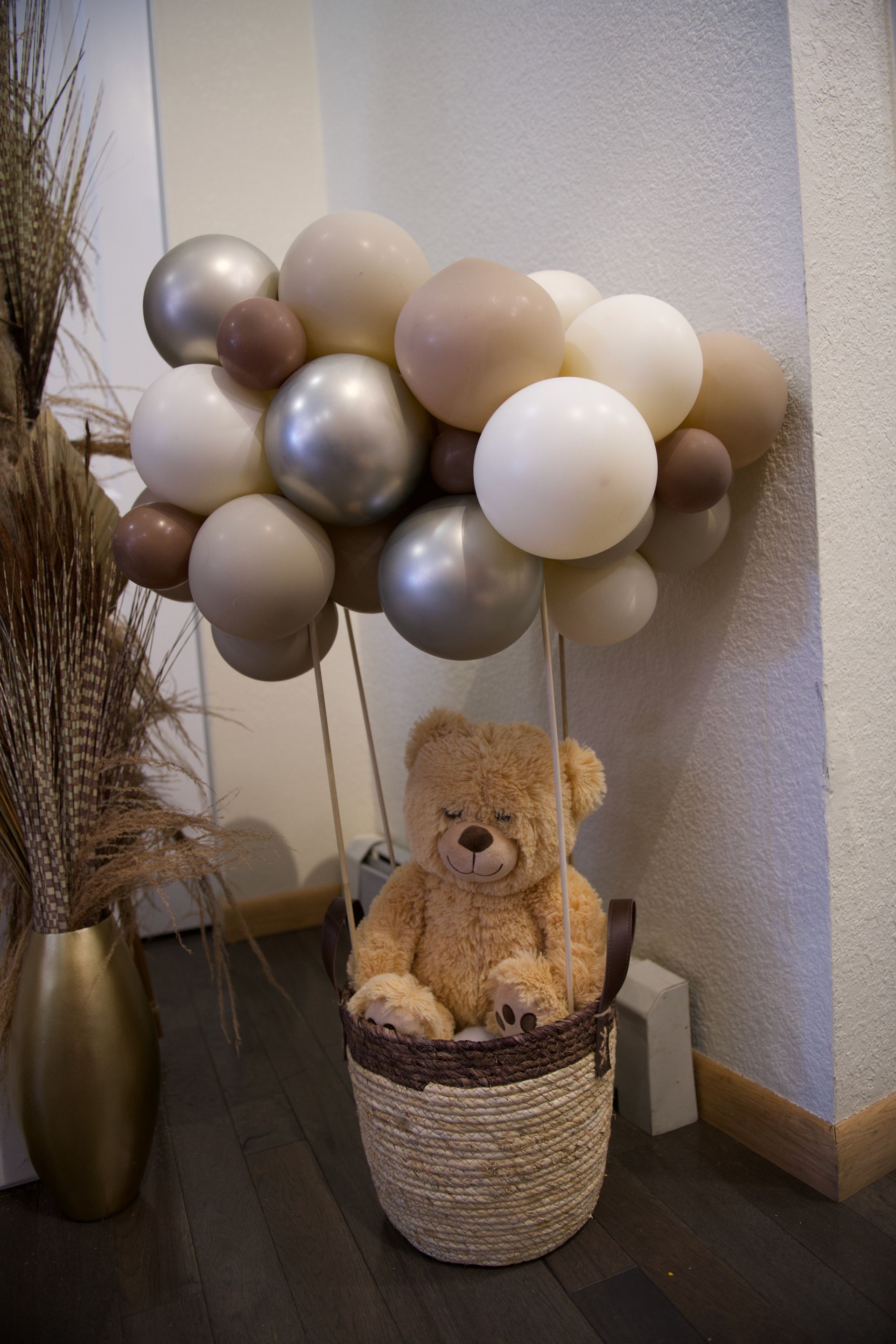 A teddy bear is sitting in a basket surrounded by balloons.