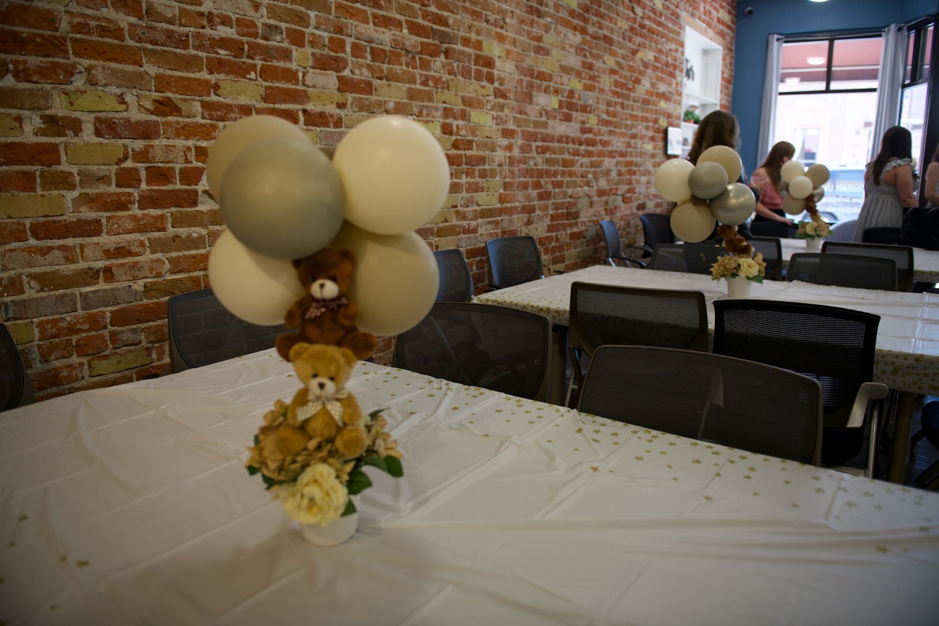 A teddy bear is sitting on top of a table with balloons.