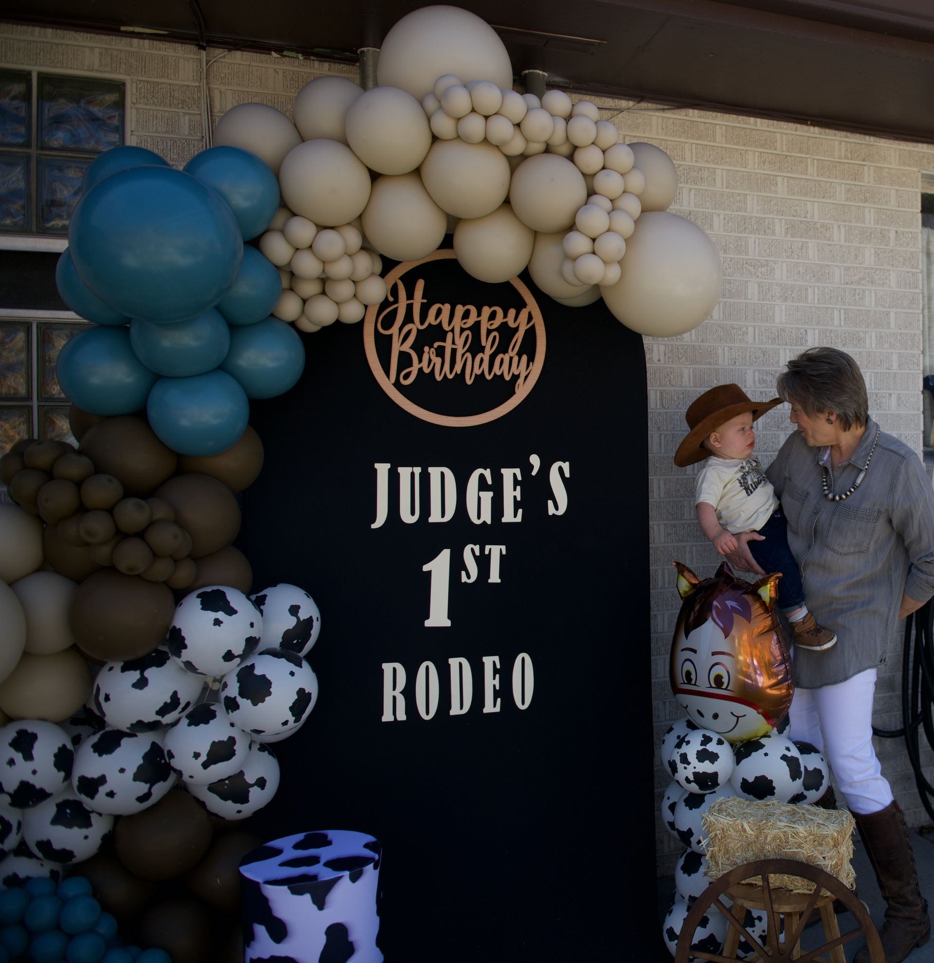 A sign that says judge 's 1st rodeo on it with balloons around.