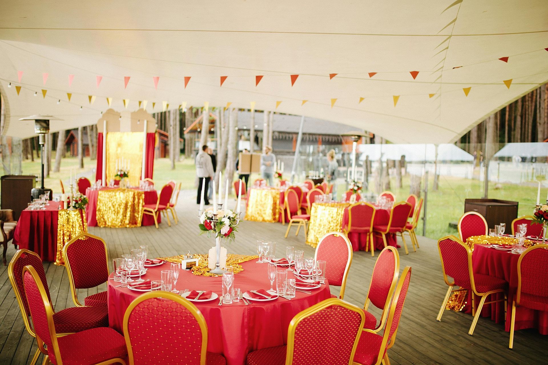 Outdoor reception with red and gold tables and chairs, under a tent decorated with pennants.