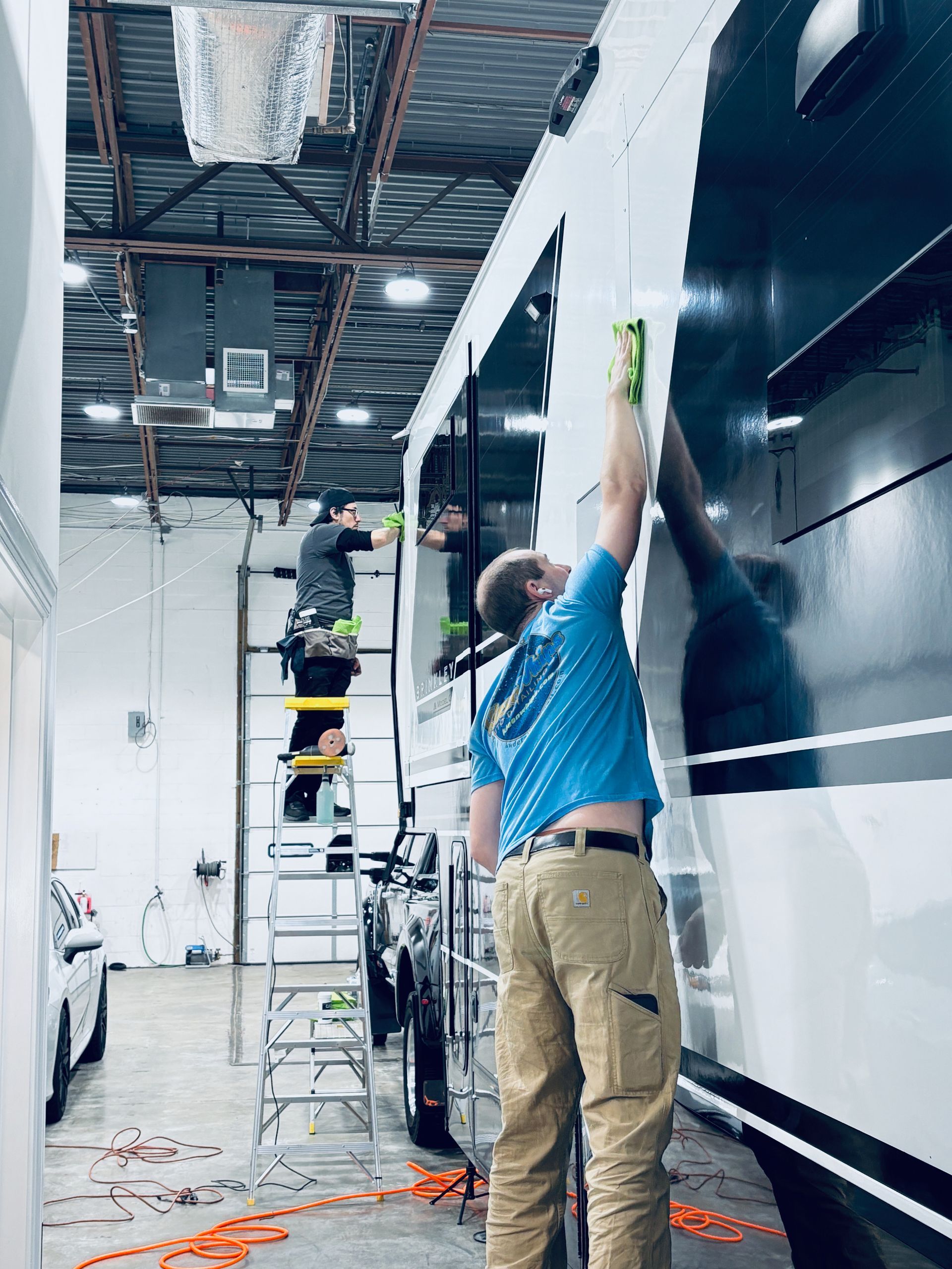 Workers on ladders painting a black-and-white wall in a bright indoor workspace.