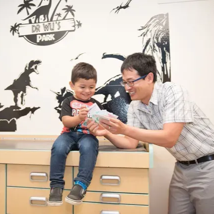 A doctor and a child look at papers on a counter with dinosaur decorations in the background.