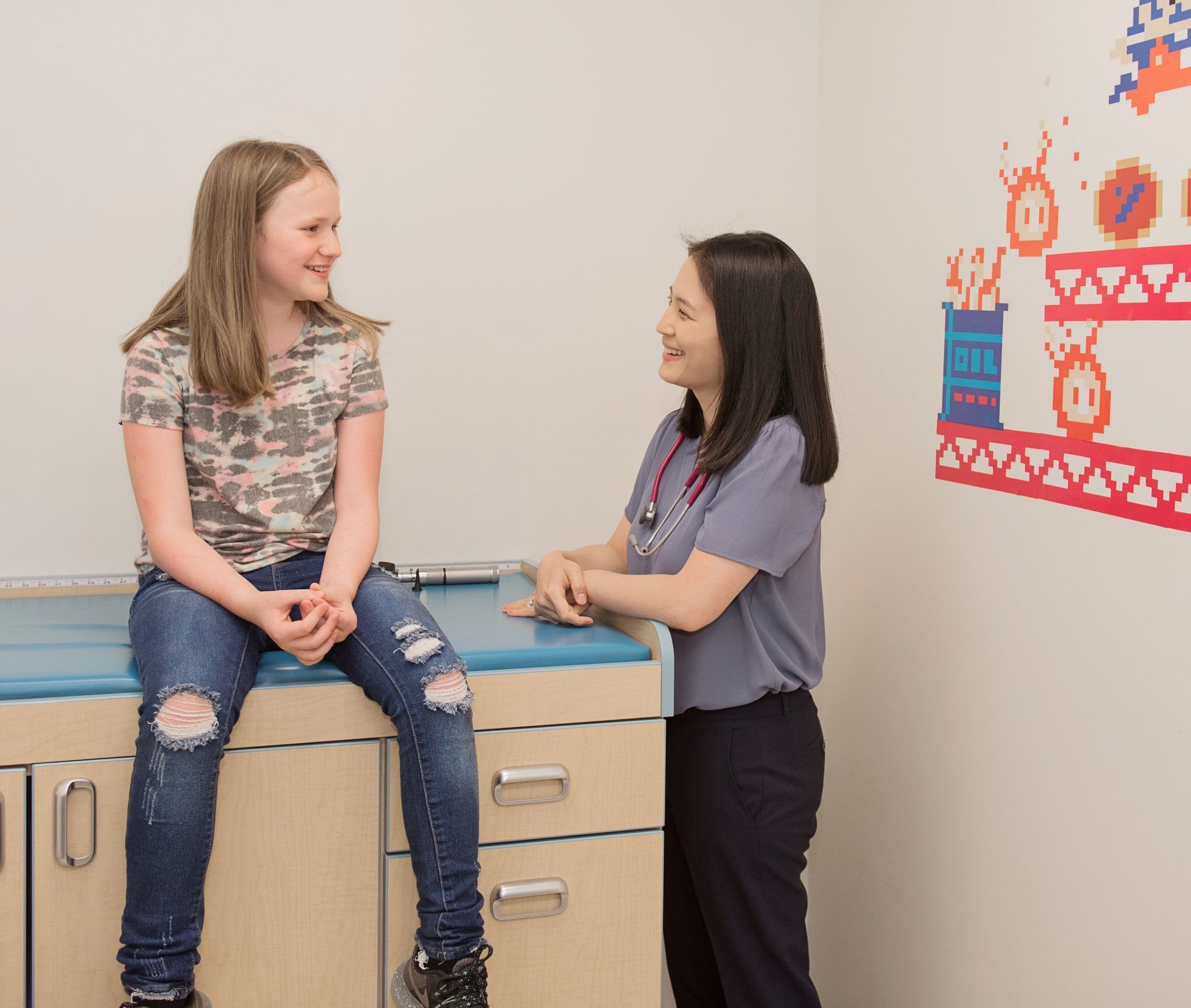 Girl sitting on exam table, talking with a doctor in a medical room.