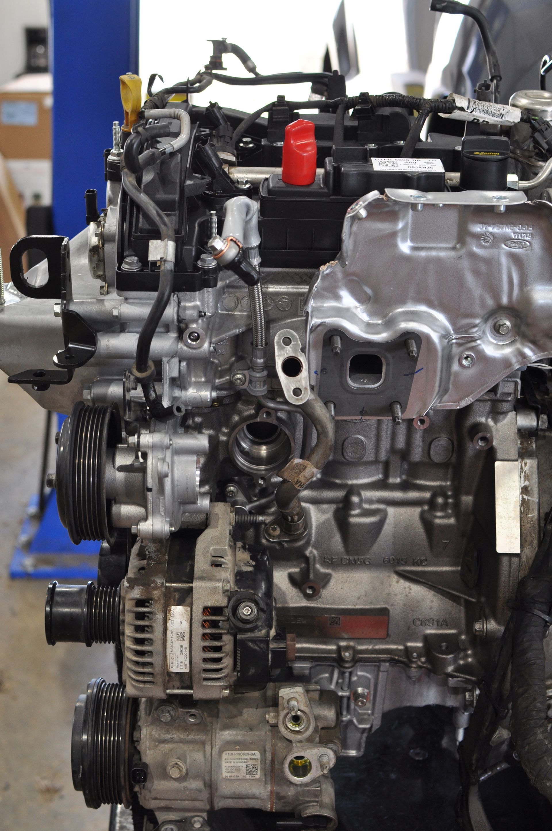Car engine on a workshop stand with exposed metal components and attached hoses.