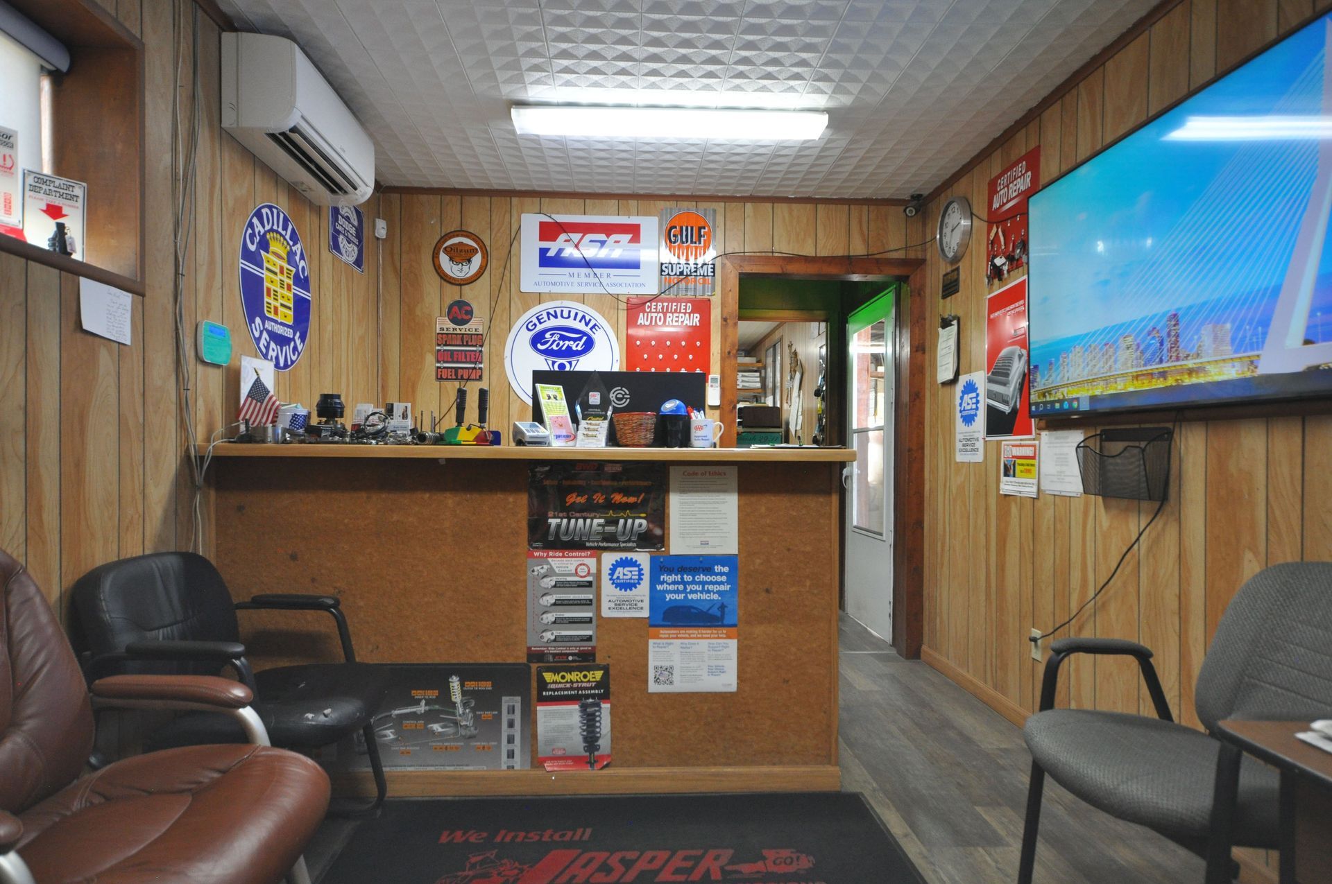 Wood-paneled waiting room with chairs, reception desk, posters, and a wall-mounted TV displaying a cityscape.