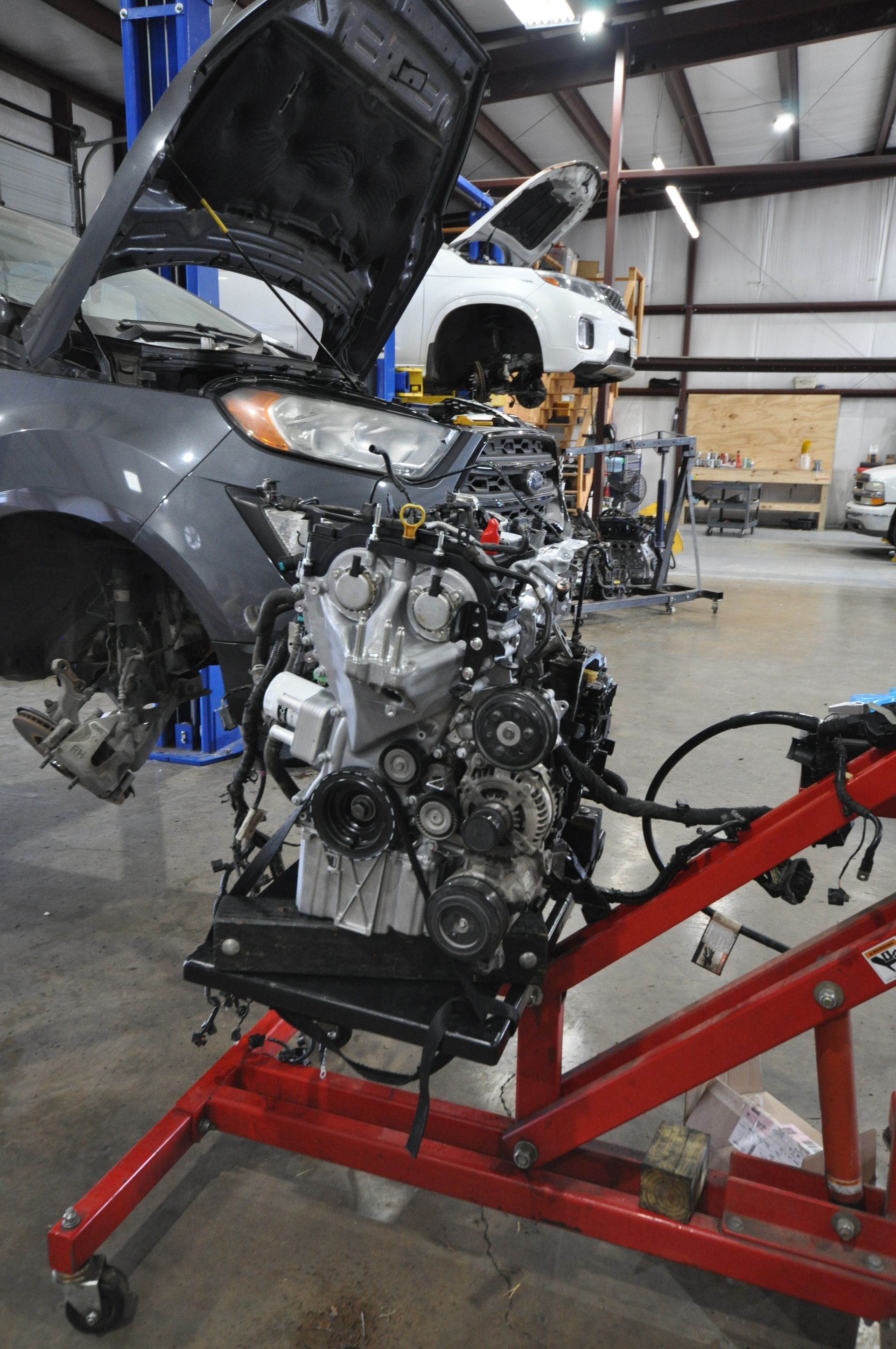 Car engine on a red stand in a garage, with a car hood open in the background.