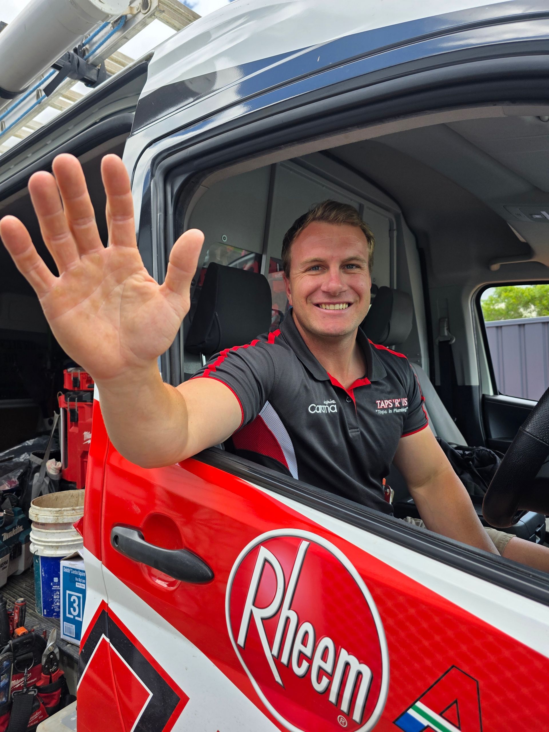Smiling driver in a red race car waves from the window, wearing a black Rheem shirt. — Taps 'R' Us in Caloundra, QLD
