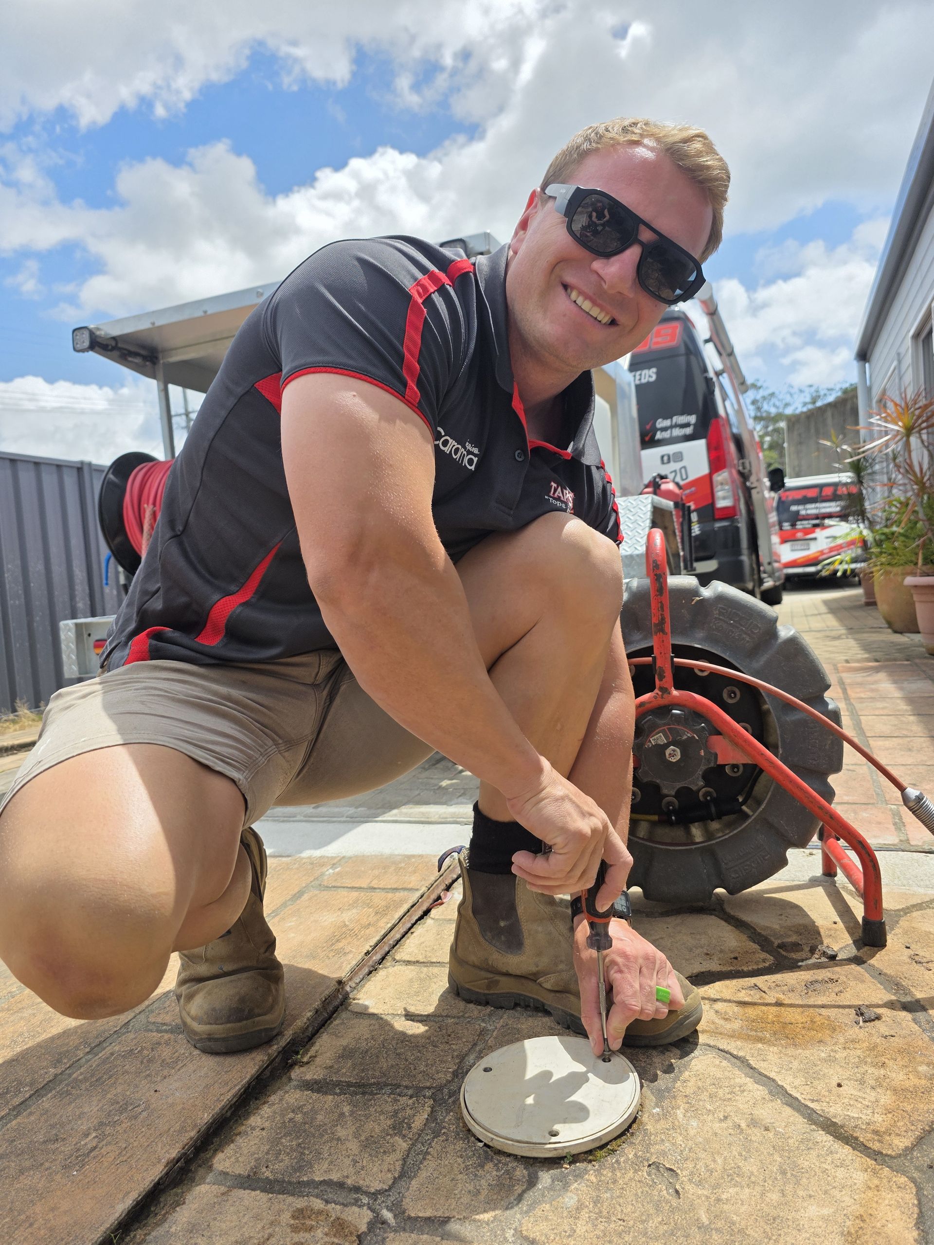 Man Crouching Outdoors Beside a Red Machine, Adjusting a Round Metal Disc — Taps 'R' Us in Kunda Park, QLD