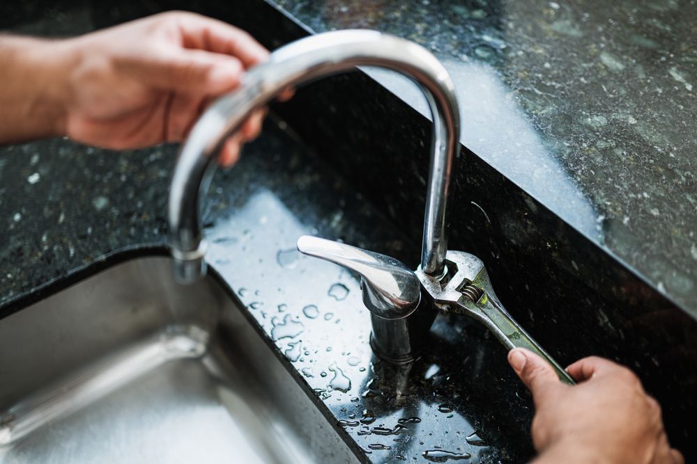Person Using a Wrench to Repair a Shiny Faucet in a Kitchen Sink — Taps 'R' Us in Kunda Park, QLD