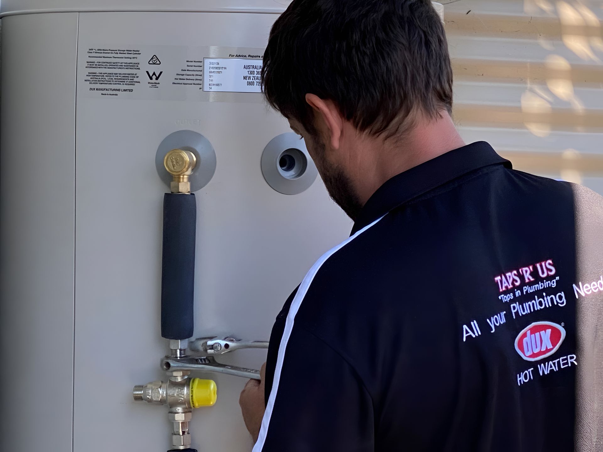 Man in Black Shirt Adjusts Plumbing on a Water Heater — Taps 'R' Us in Kunda Park, QLD