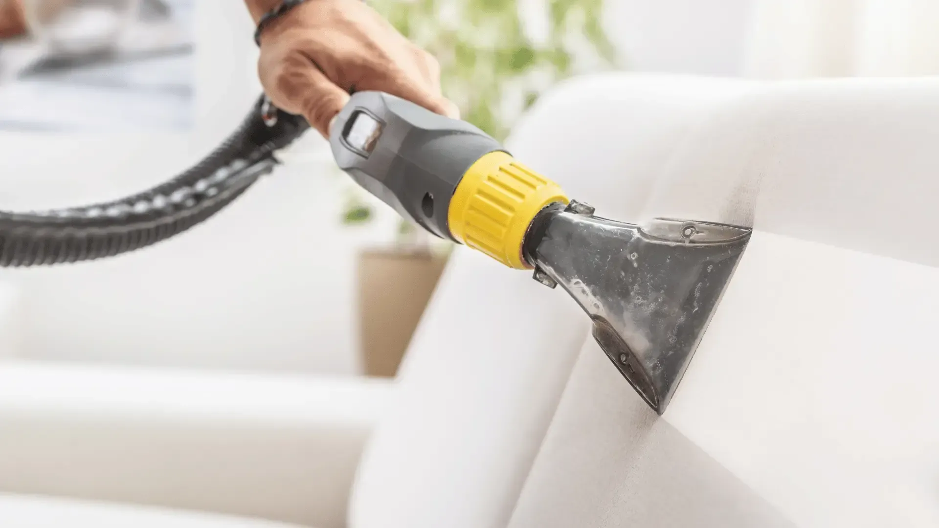 A person is cleaning a couch with a vacuum cleaner.