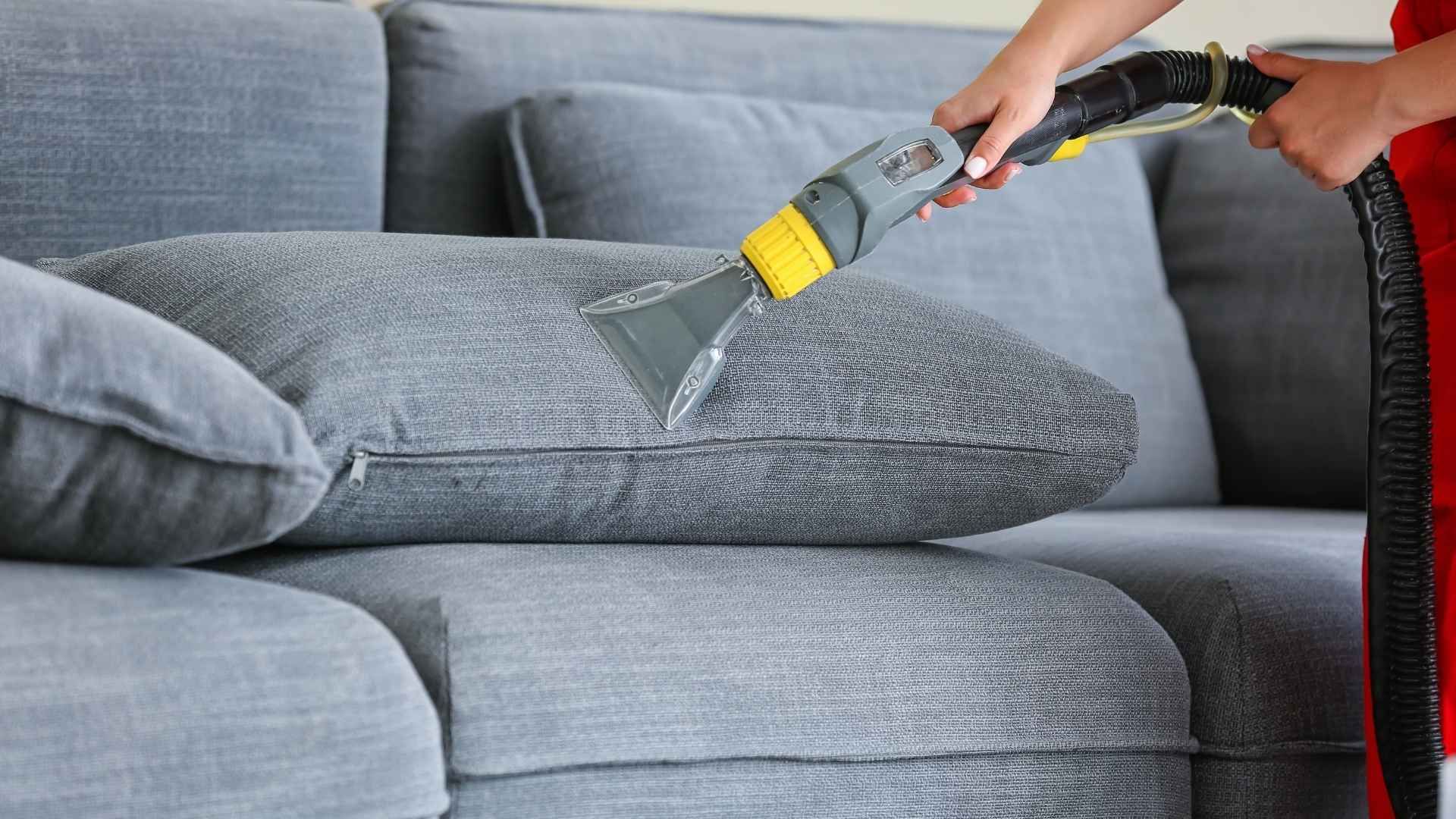 A person is cleaning a couch with a vacuum cleaner.